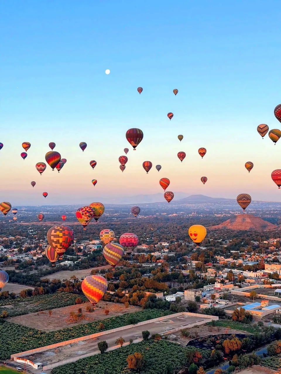 A fleet of hot air balloons filling the sky over the Teotihuacan valley in the blue hour