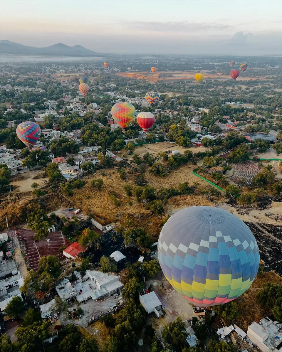 A hot air balloon descending beside the Pyramid of the Moon among the trees of Teotihuacan