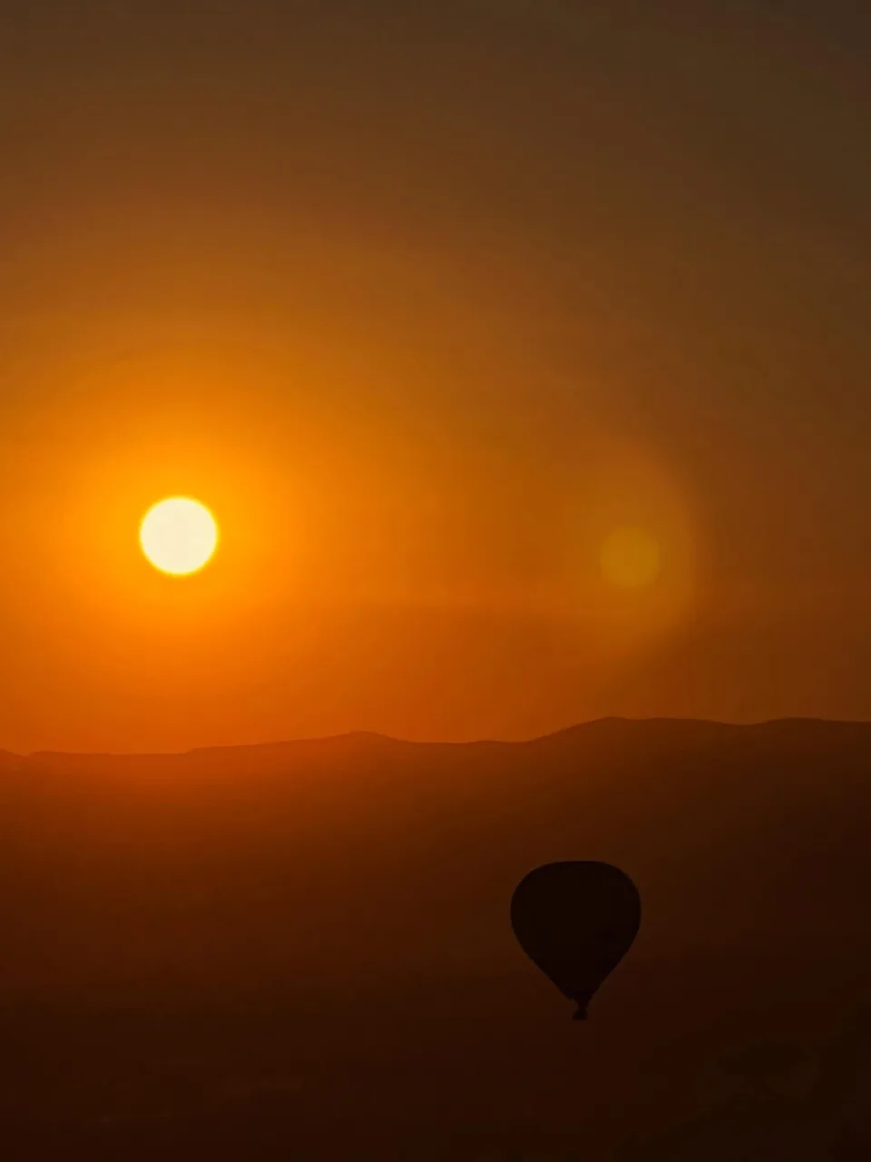 A hot air balloon in silhouette against an orange sunrise over Teotihuacan