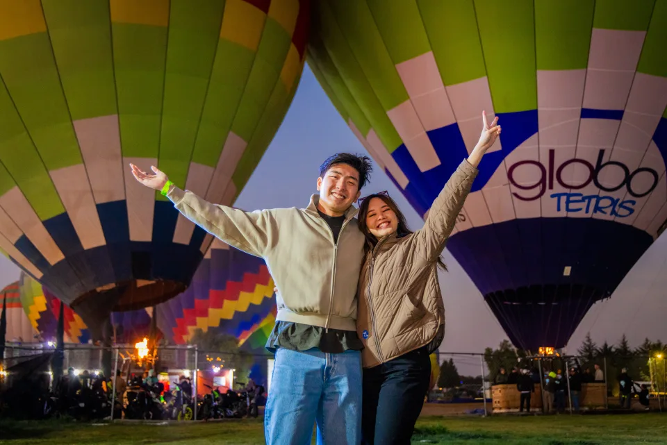 Pareja emocionada con los brazos en alto ante globos encendidos antes del amanecer