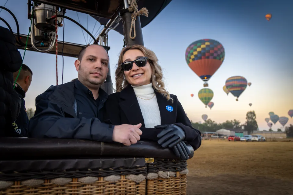 Pareja dentro de la canastilla con muchos globos elevándose al amanecer