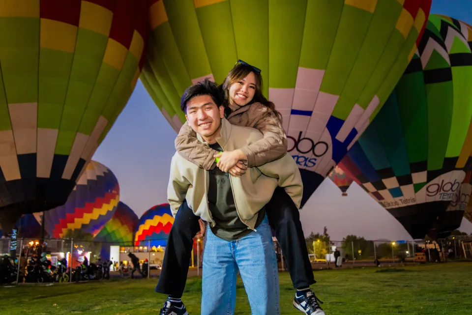 Pareja jugando a caballito frente a globos encendidos al amanecer