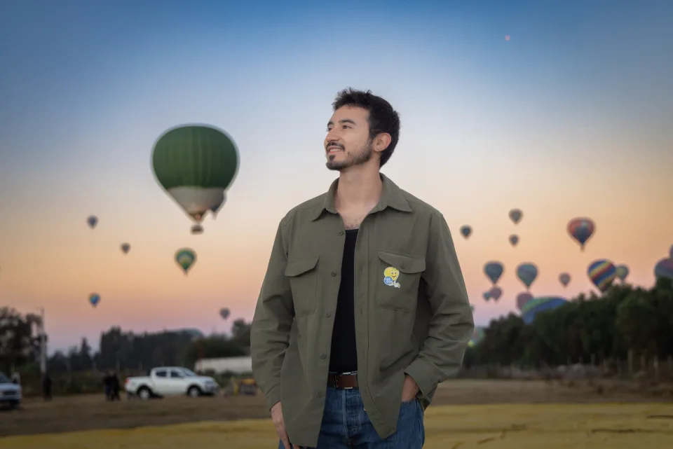 Hombre de pie en el campo mientras muchos globos cruzan el cielo del amanecer en Teotihuacán