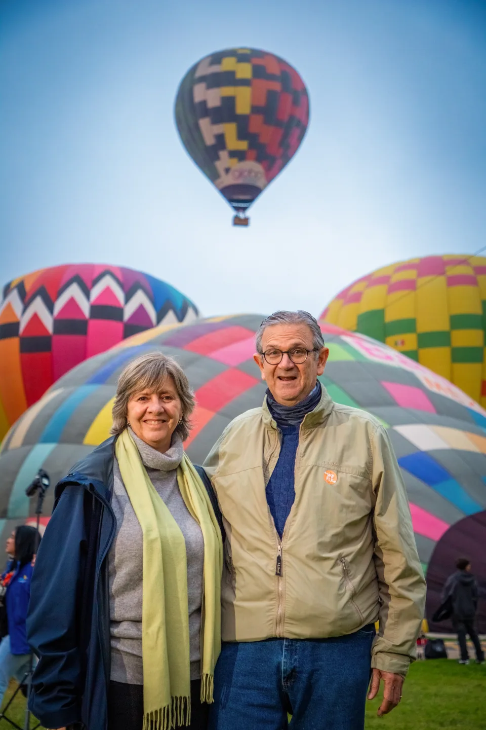 Pareja mayor sonriente con coloridos globos inflándose detrás al amanecer