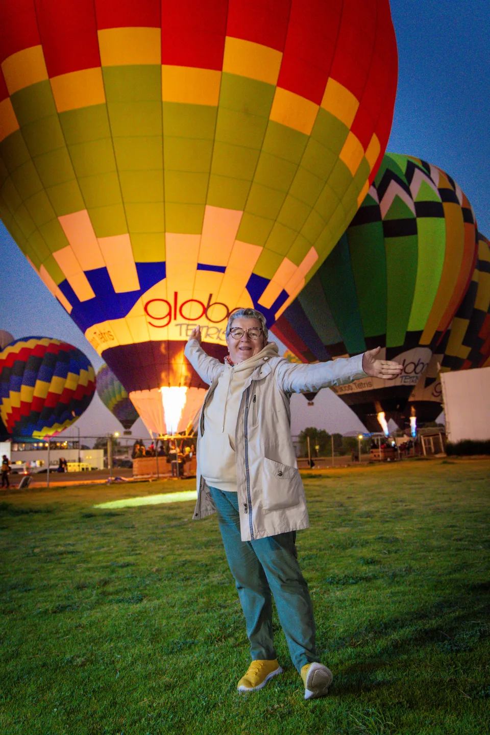 Mujer mayor radiante con los brazos abiertos ante globos encendidos al amanecer