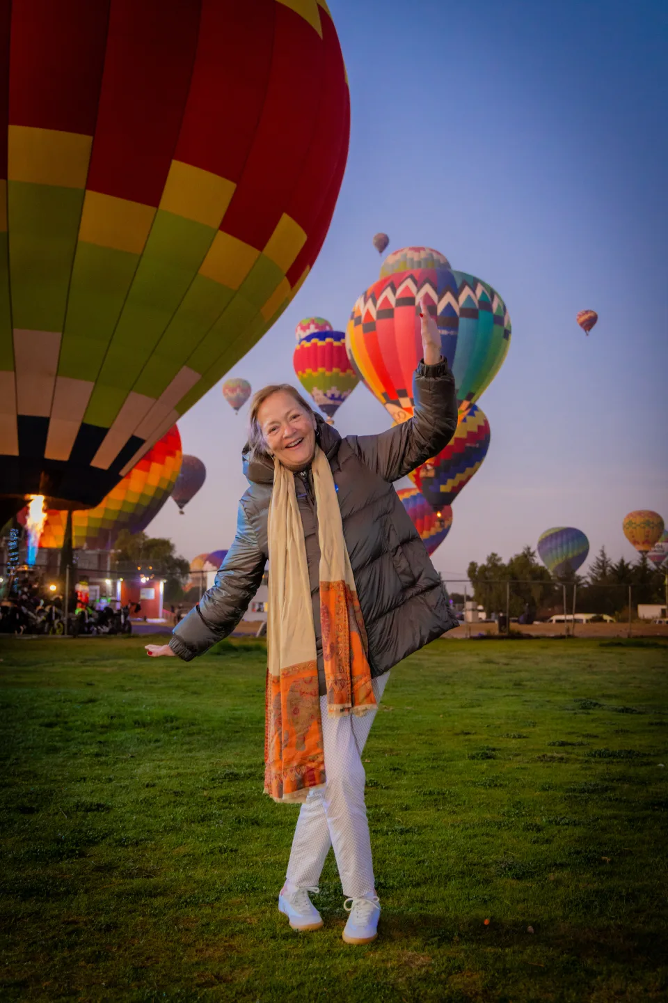 Mujer mayor alegre posando con muchos globos al amanecer