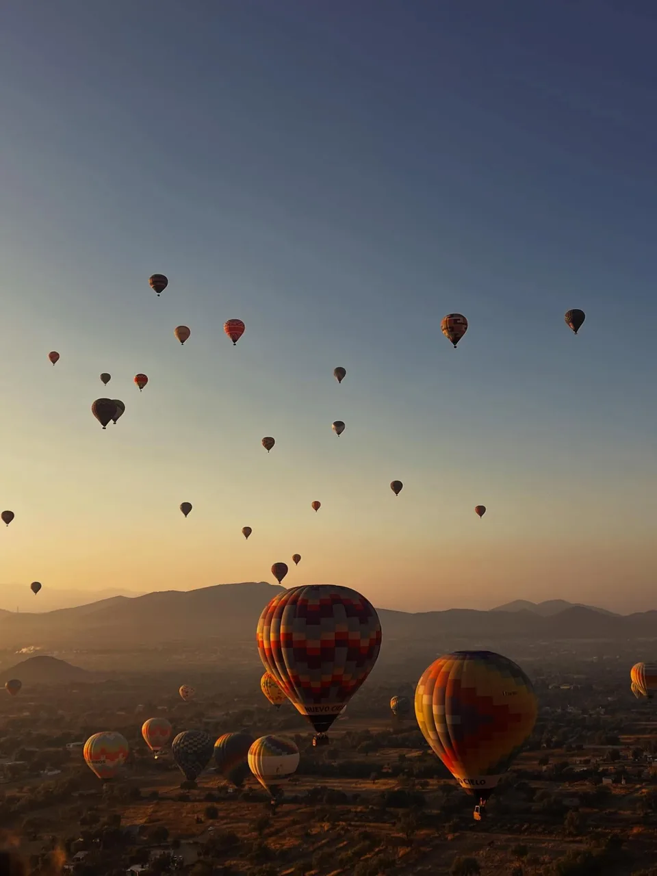 A passenger photographs the balloons rising over the hills at first light