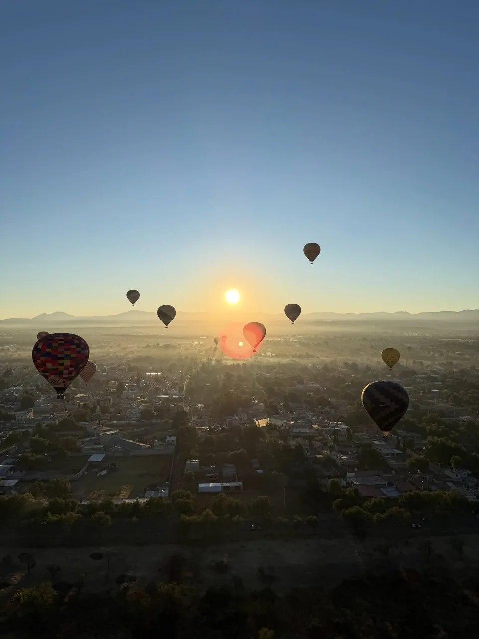 The sun breaking the horizon behind hot air balloons over Teotihuacan
