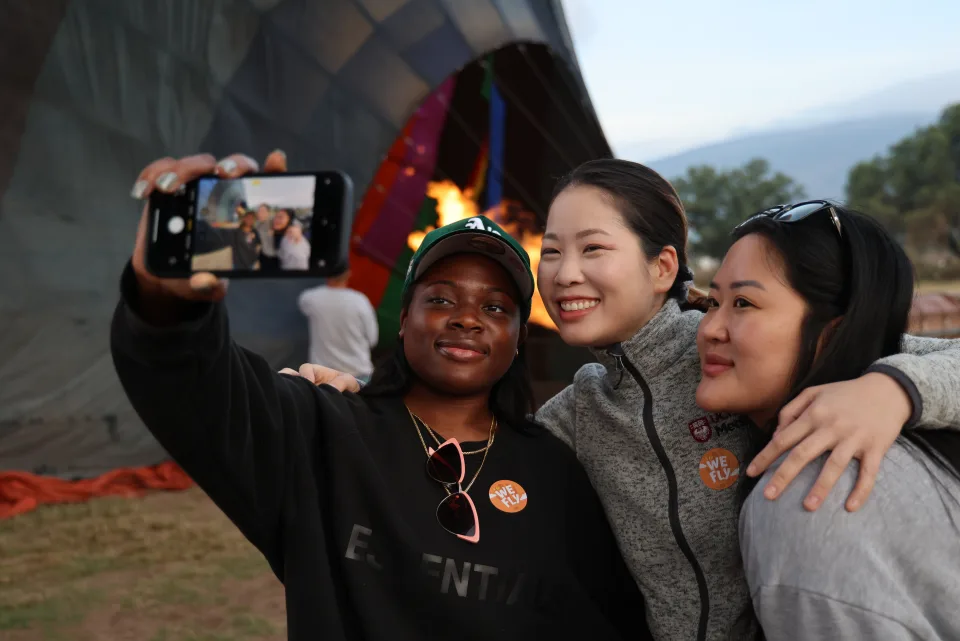 Tres amigas tomándose una selfie junto a un globo encendido al amanecer