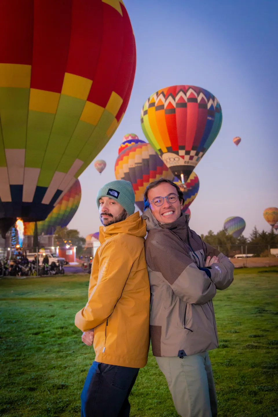 Dos amigos posando espalda con espalda con globos coloridos al amanecer