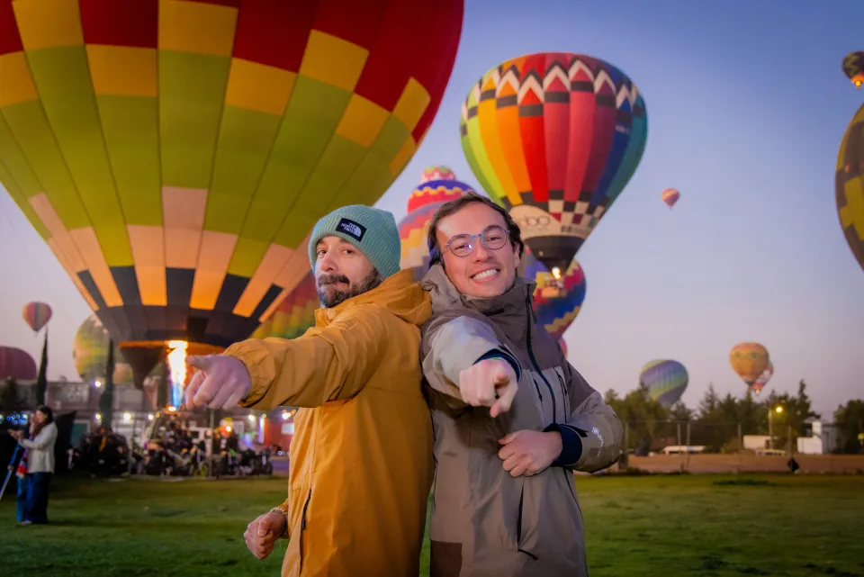 Dos amigos señalando a la cámara con globos del amanecer detrás