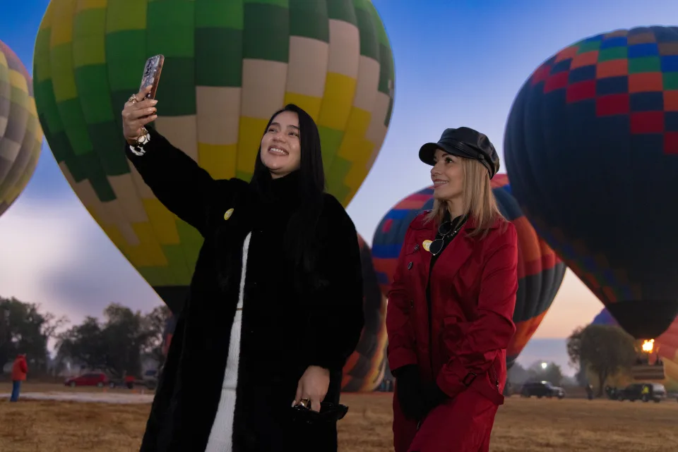 Dos mujeres tomándose una selfie con globos en el campo a primera luz
