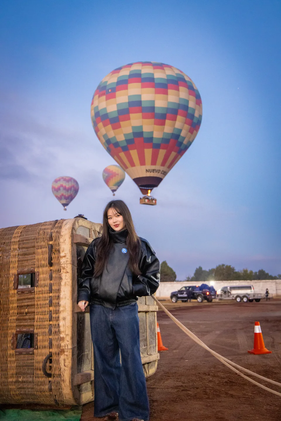 Mujer junto a una canastilla mientras otro globo flota arriba al amanecer