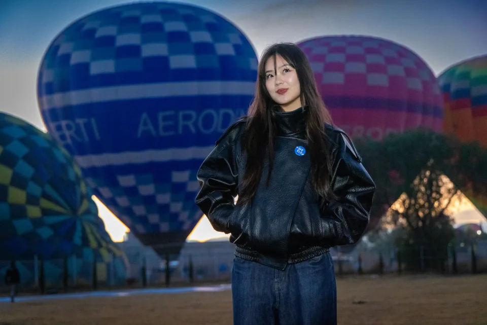 Mujer con chaqueta de cuero frente a un globo azul al amanecer