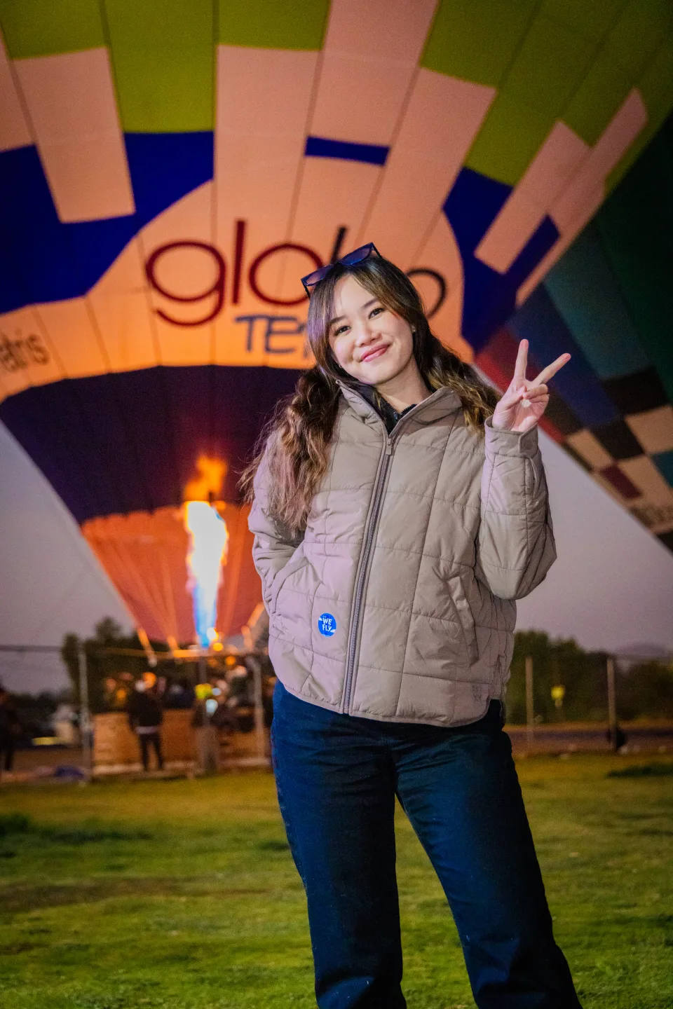 Joven haciendo el signo de paz ante un globo encendido y la llama del quemador