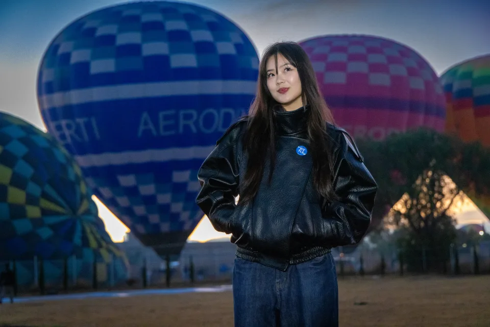 Mujer posando ante un globo azul en el campo de despegue al amanecer
