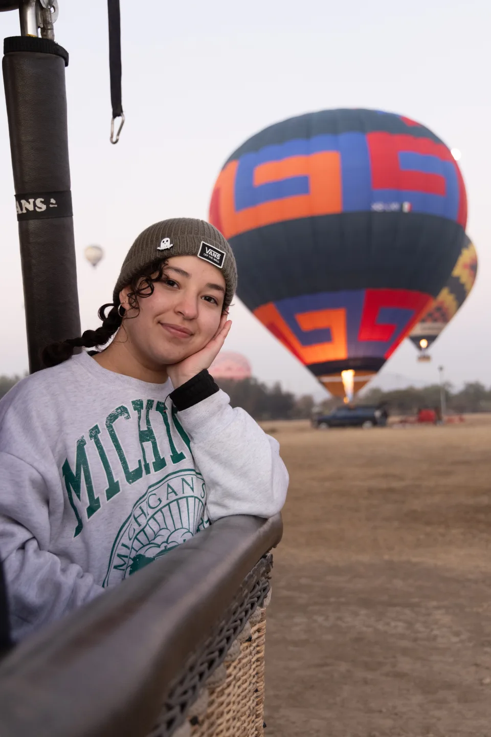 Mujer apoyando la cabeza en el borde de la canastilla con un globo en el campo al amanecer