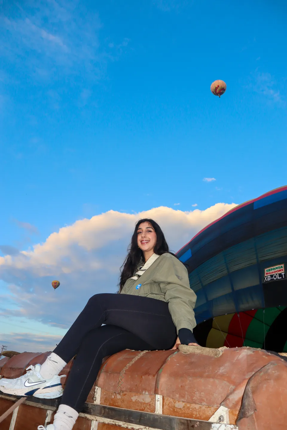 Mujer sentada sobre la canastilla con globos flotando en un cielo azul despejado