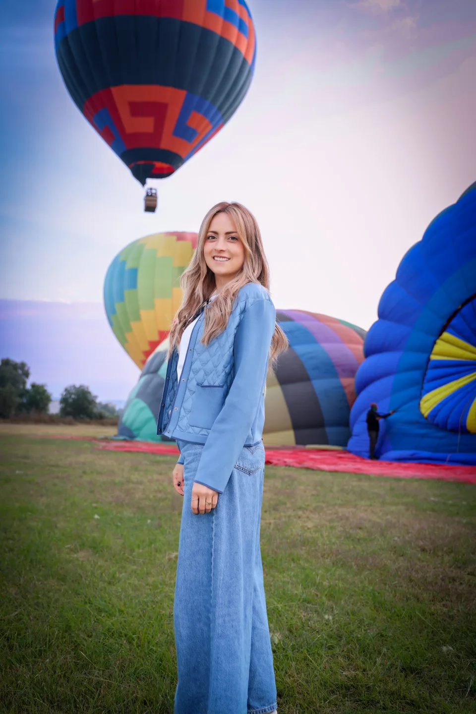 Mujer de pie en el campo de despegue con un globo elevándose detrás al amanecer