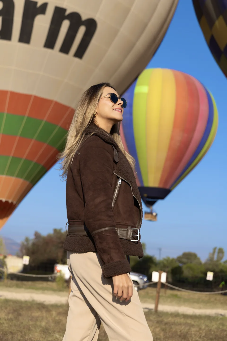 Mujer con lentes de sol caminando junto a coloridos globos bajo un cielo azul