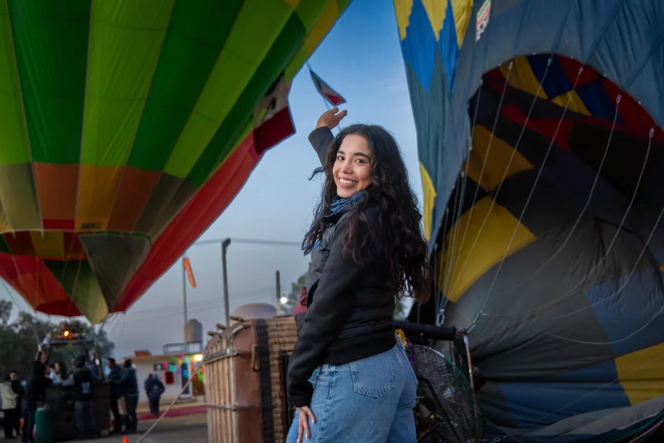 Mujer sonriente saludando entre dos grandes globos inflándose al amanecer