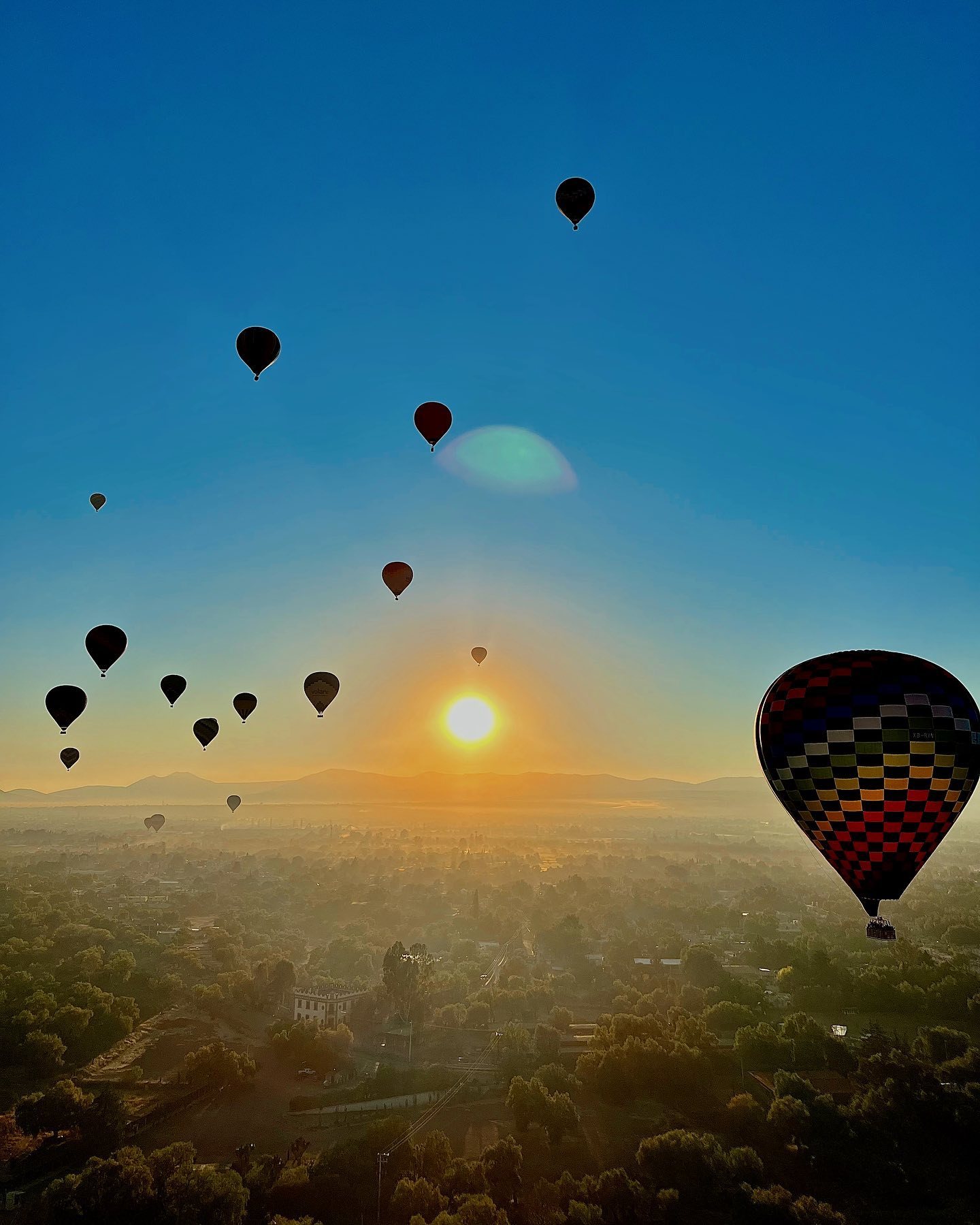 The sun breaking the horizon behind a line of hot air balloons over Teotihuacan